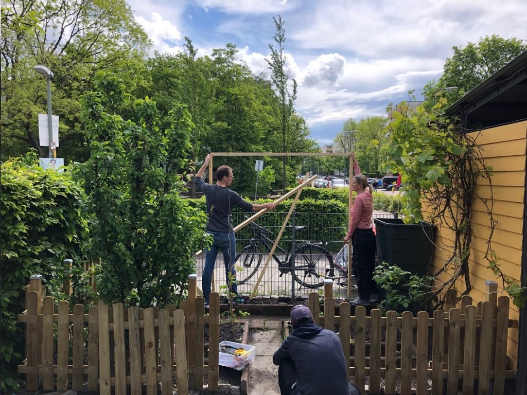 Ein Mann und eine Frau bauen ein Gerüst aus Holz im Garten der Kita auf