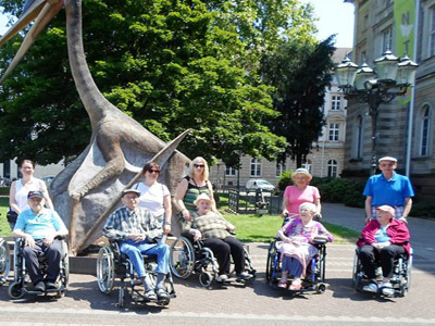 Eine Gruppe von Menschen mit und ohne Behinderung posieren vor dem Dinosaurier am Naturkundemuseum in Karlsruhe.