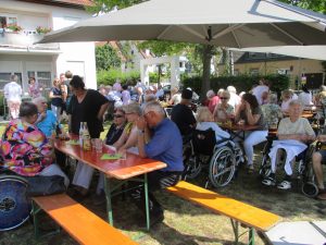 Viele Menschen sitzen an Biertischgarnituren unter Zelten.