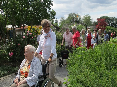 Bewohnerinnen des Seniorenzentrums und Mitarbeiterinnen spazieren durch die Gartenanlage des Gartenbauvereins