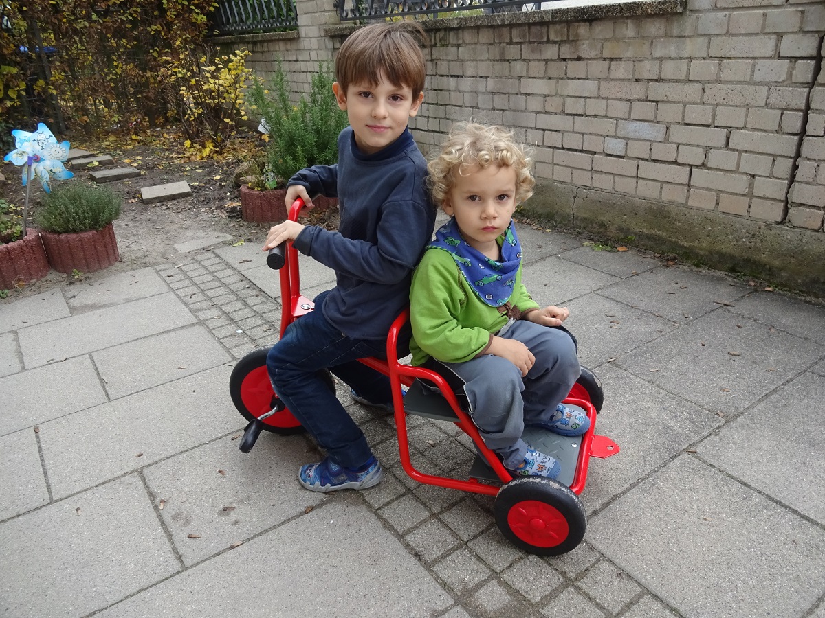 Zwei Kita Kinder sitzen auf dem geschenkten Dreirad