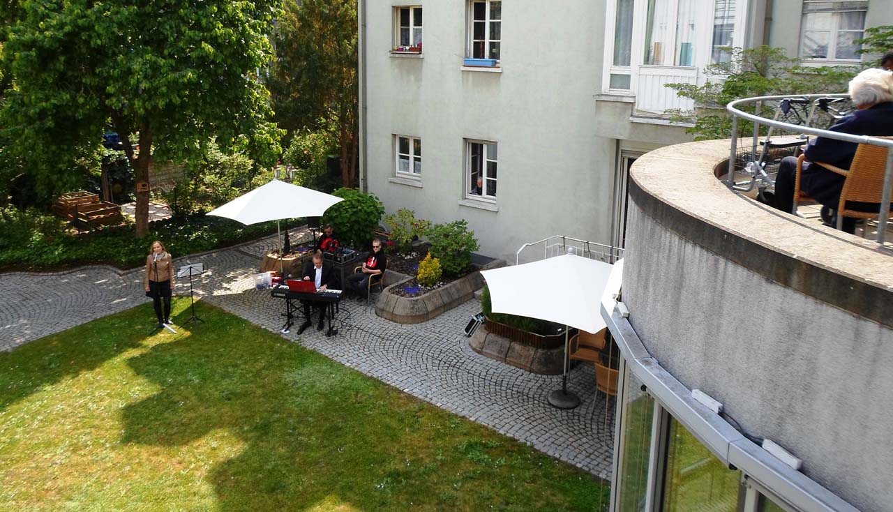 Zwei Menschen stehen im Garten und schauen nach oben zu einem Balkon.