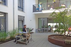 Ein Mann sitzt in einem Hof und spielt auf einer Zieharmonika.