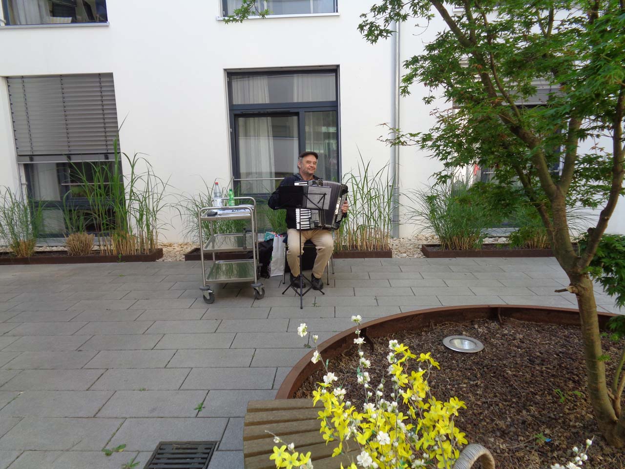 Ein Mann sitzt in einem Hof und spielt auf einer Zieharmonika.