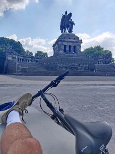 Blick auf ein Bein und ein Fahrrad vor einem Denkmal