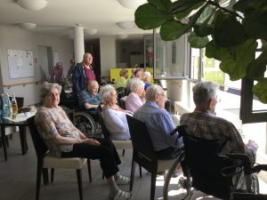 Senior*innen sitzen vor dem Fenster und hören Live-Musik.