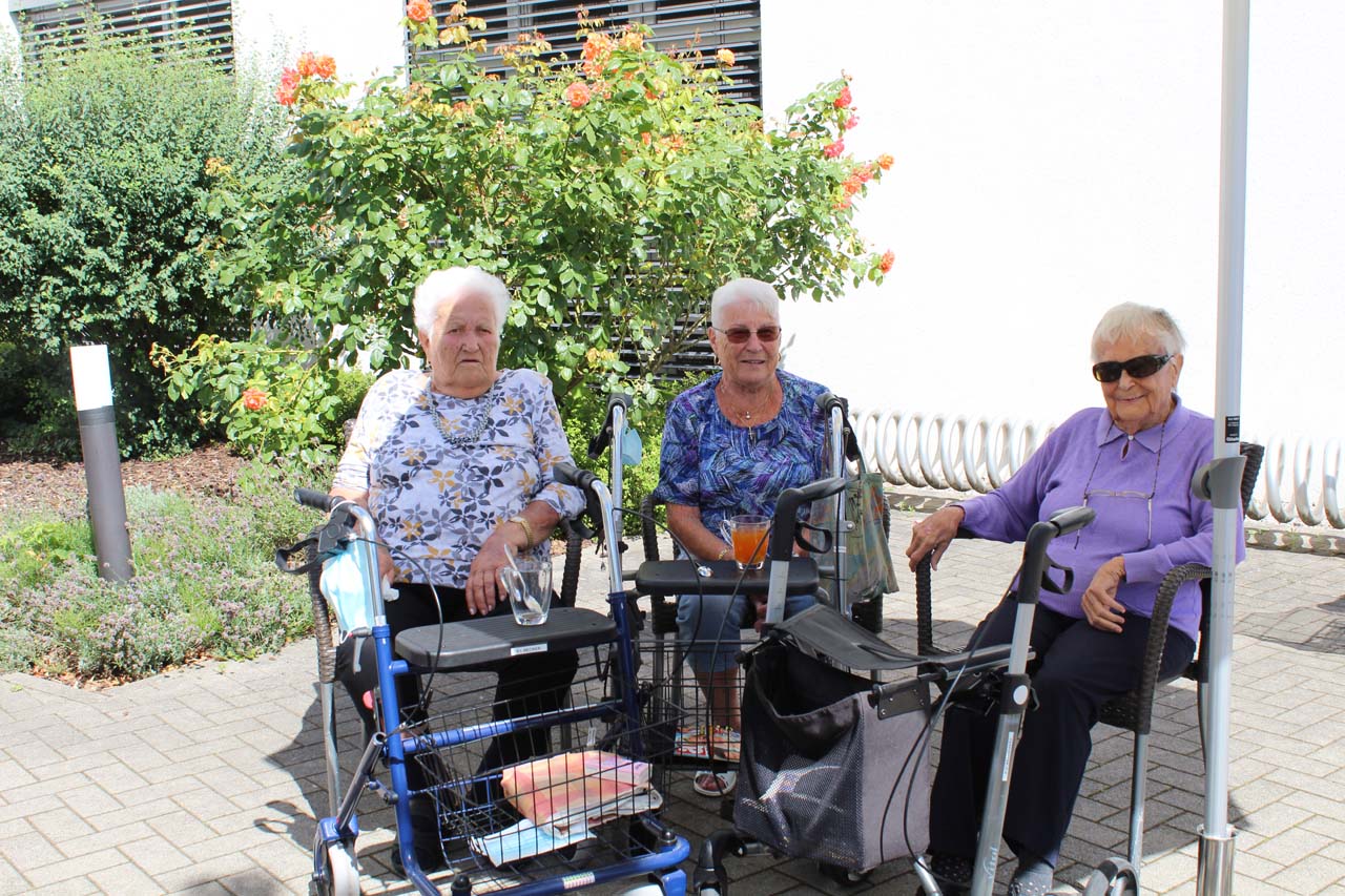 Drei Senior*innen sitzen im Freien und lachen.
