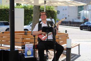 Ein Mann sitzt mit einer Gitarre auf einer Bank.