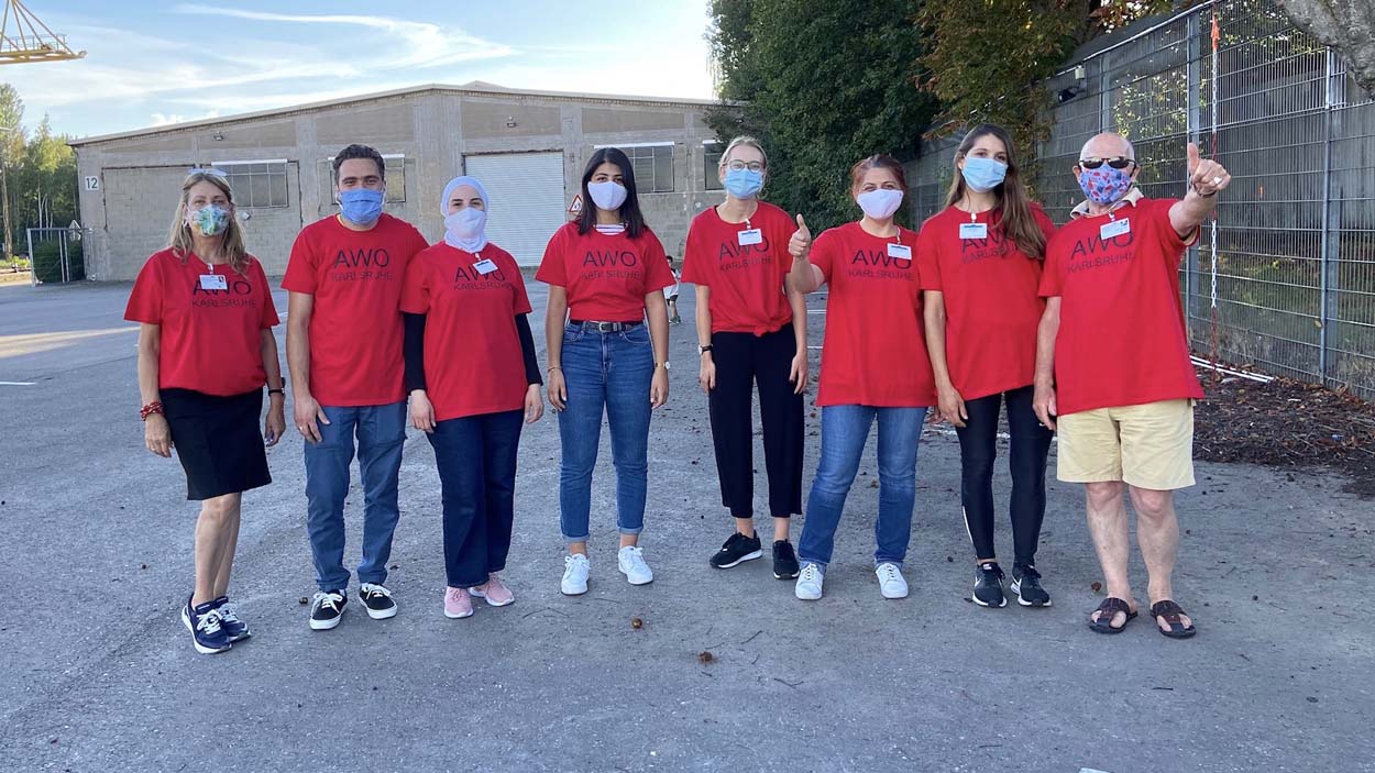 Acht Menschen in roten Tshirts und Masken stehen als Gruppe zusammen.