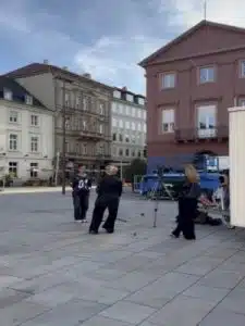Drei Frauen filmen ein Interview auf einem Platz mit historischen Gebäuden im Hintergrund.