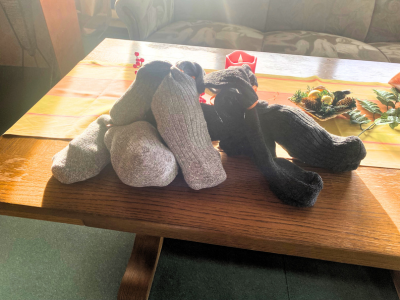Mehrere Paar Socken liegen gefaltet auf einem Holztisch. Die Socken sind unterschiedlich farbig. Auf dem Tisch liegt eine weihnachtliche Tischdekoration mit kleinen Zweigen und Anhängern.