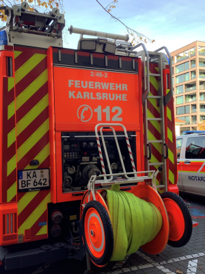 Rückseite eines Feuerwehrfahrzeugs der Feuerwehr Karlsruhe. Gut sichtbar sind die orangefarbenen Warnmarkierungen, die Nummer 112, aufgerollte Schläuche und offene Technikfächer.