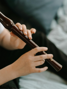 Nahaufnahme einer Person, die eine dunkle Altblockflöte spielt. Die Hände greifen konzentriert die Tonlöcher, im Hintergrund ist ein unscharfer, weicher Stoff sichtbar.