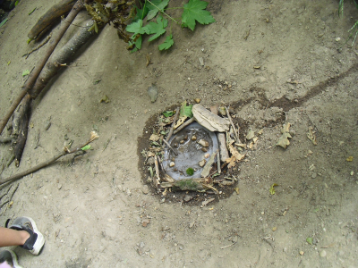 Im Waldboden ist ein rundes Naturkunstwerk ausgelegt. Es besteht aus Stöcken, Blättern, kleinen Steinen und Früchten. Daneben sind Kinderfüße zu sehen.