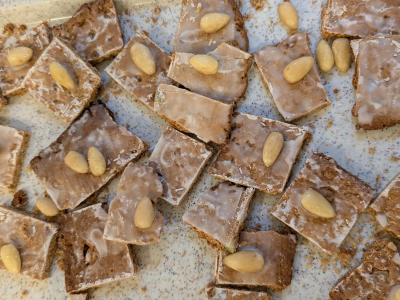 Quadratische Gebäckstücke mit Zuckerguss und Mandeln liegen dicht an dicht auf einem Blech.