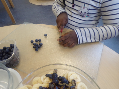 Ein Kind in der Kita schneidet konzentriert Blaubeeren für einen Obstsalat zum deutsch-französischen Tag.