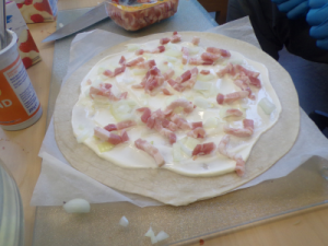 Nahaufnahme eines traditionell belegten Elsässer Flammkuchens mit Speck und Zwiebeln vor dem Backen