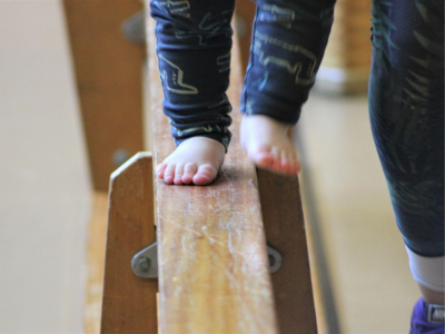 Kinderfüße balancieren barfuß über eine schmale Holzbank zur Schulung von Gleichgewicht und Koordination im Kita-Alltag.