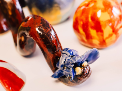Nahaufnahme einer handgefertigten Keramikfigur in kräftigen Farben, umgeben von weiteren Keramikobjekten.
