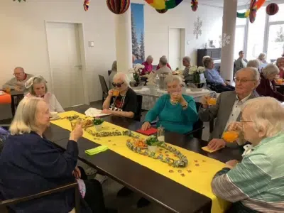Senior*innen sitzen an festlich mit gelben Läufern dekorierten Tischen und stoßen mit Fruchtbowle auf den Rosenmontag an.