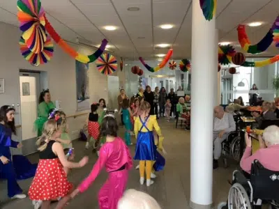 Eine bunte Kinder-Tanzgruppe in farbenfrohen Kostümen führt im dekorierten Restaurant des AWO Seniorenzentrums einen Schautanz auf.
