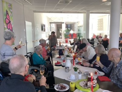 Bewohner*innen stoßen im Seniorenzentrum Grünwinkel mit Getränken an und genießen Kuchen in geselliger Runde beim Geburtstagskaffee.
