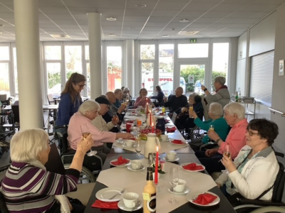 Lange Kaffeetafel im Seniorenzentrum Grünwinkel mit Bewohner*innen, die gemeinsam Geburtstag feiern und Kuchen sowie Getränke genießen.