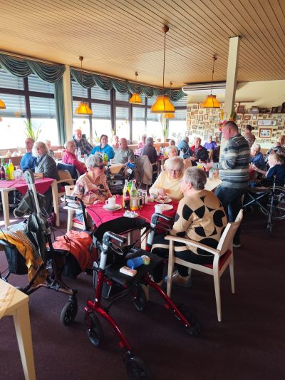 Bewohner*innen sitzen gemeinsam an gedeckten Tischen beim Osterfest im Seniorenzentrum Haus am Blumentor