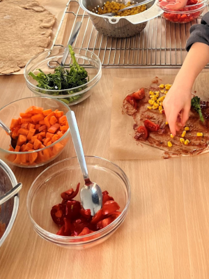 Schüsseln mit geschnittenem Gemüse wie Paprika, Karotten und Brokkoli stehen auf einem Tisch neben einem vorbereiteten Teig.