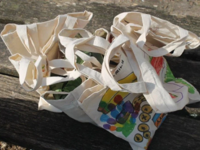 Mehrere bemalte Stofftaschen mit bunten Obst- und Gemüsemotiven liegen auf einer Holzbank.
