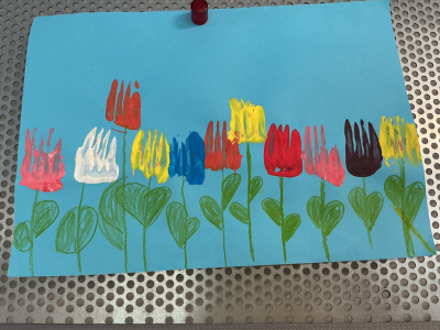 Eine Zeichnung auf hellblauem Papier. Eine Reihe bunter Tulpenblüten (rot, weiß, gelb, blau, rosa) ist mit der Gabel-Drucktechnik gestaltet worden. Die Zinken-Abdrücke sind deutlich sichtbar. Die grünen Stiele und Blätter sind handgezeichnet.