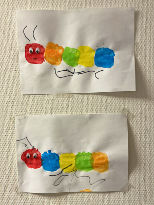 Zwei waagerechte Kinderzeichnungen übereinander. Jede Zeichnung zeigt eine Raupe, die aus farbigen, mit Schwämmen gedruckten Kreisen (rot, orange, grün, gelb, blau) besteht. Die Raupen haben Wackelaugen und handgezeichnete Beine und Fühler.