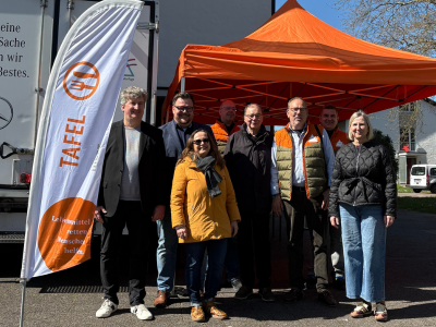 • Gruppe von Engagierten vor einem Tafel-Fahrzeug und Pavillon bei der Lebensmittelausgabe im Stadtteil.
