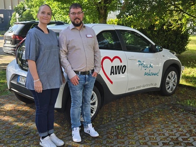 Anna Kinghorne, Sachgebietsleitung und Bela Leko, Pflegedienstleitung, stehen vor einem AWO-Fahrzeug.