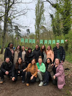 Das Team der AWO Kita Mikado Karlsruhe posiert für ein Gruppenfoto im Wald unter einer "KITA MIKADO" Wimpelkette.