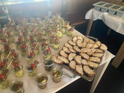 Buffettisch mit kleinen Gläsern (Fingerfood, z. B. Salate) und belegten Brotscheiben auf Tabletts, alles ordentlich angerichtet.