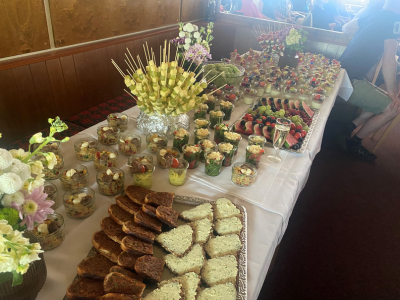 Langes Buffet mit verschiedenen Häppchen, Broten und dekorierten Gläsern, Blumenschmuck und arrangierte Speisen auf weißer Tischdecke.