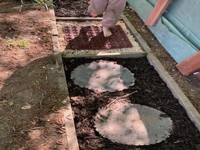 Ein Kind testet den Barfußpfad mit Holzscheiben, Steinen und Rindenmulch im Kita-Garten.