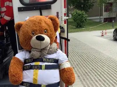 Teddybär in weißem Kittel und Sicherheitsgurt auf einer Rettungsliege vor einem Rettungsfahrzeug beim Teddy-Krankenhaus im Städtischen Klinikum Karlsruhe