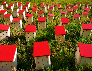 Viele Insektenhotels mit rotem Dach auf einer grünen Wiese.