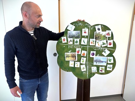 Ein Mitarbeiter präsentiert einen Lernbaum mit Karten zu Jahreszeiten, Pflanzen und Tieren im Rahmen des Klimaspürnasen-Projekts in der Kita Pamina.