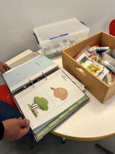 Arbeitsmaterialien des Klimaspürnasen-Projekts: Ein Ordner mit Bildkarten zu Natur und Jahreszeiten sowie Bastelutensilien auf einem Tisch in der Kita Pamina.