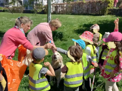 Kinder und Erzieherinnen der Kita Aufwind stehen im Halbkreis um den Golden Retriever Malka; eine Erzieherin hält einen Müllgreifer in der Hand.