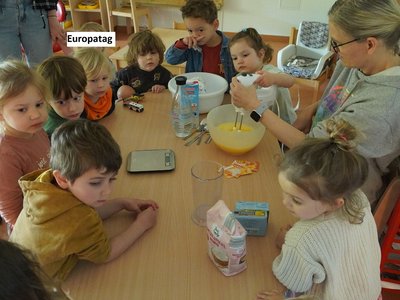 Kinder der Kita les petits amis sitzen gemeinsam am Tisch und bereiten Zutaten für das Europatag-Menü vor.