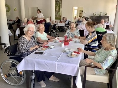 Bewohnerinnen des Seniorenzentrums Grünwinkel sitzen an einem festlich gedeckten Tisch und genießen Erdbeerkuchen und Getränke beim Erdbeerfest.