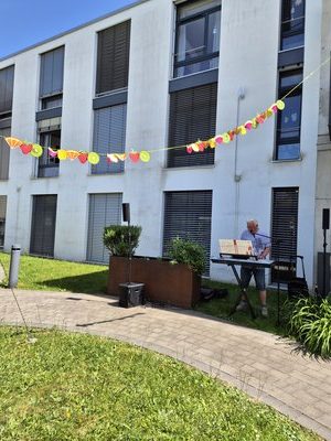 Keyboarder spielt im Innenhof des Seniorenzentrums Knielingen vor einer Obstgirlande; Yamaha-Keyboard mit Mikrofon und Lautsprechern.