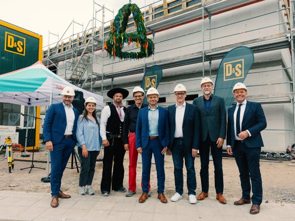 Richtfest an der Johestraße in Karlsruhe-Oberreut: Baubeteiligte, Vertreter*innen der Volkswohnung und der Stadt Karlsruhe vor dem Rohbau der künftigen Kita Ringelblume – mit dem traditionellen Richtkranz auf dem Gerüst.