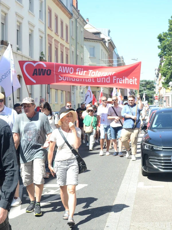 Demonstrationszug in einer Wohnstraße: Vorne wird ein rotes AWO-Banner mit der Aufschrift „AWO für Toleranz, Solidarität und Freiheit“ getragen, dahinter laufen zahlreiche Teilnehmende bei sonnigem Wetter.
