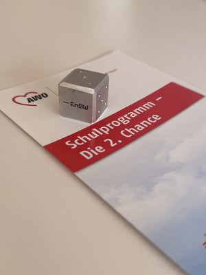 Kleiner Aluminiumwürfel mit EnBW-Logo auf einer Broschüre zum Schulprogramm „Die 2. Chance“.