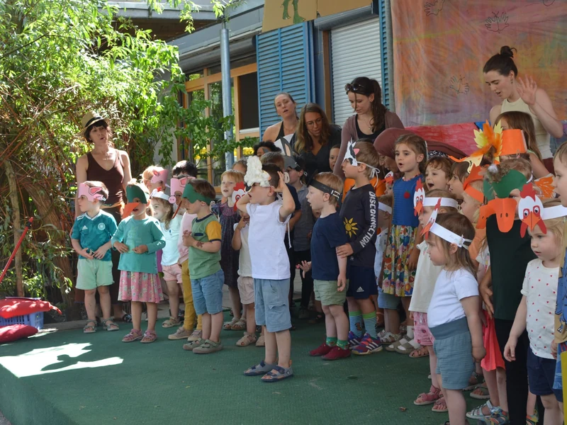 Kinder und pädagogische Fachkräfte bei einer Aufführung mit selbst gebastelten Tiermasken beim Sommerfest.